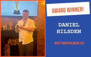 The winner of the July networking question at Cambridge's networking meeting, holding the trophy and standing in front of a screen which also displays a trophy.