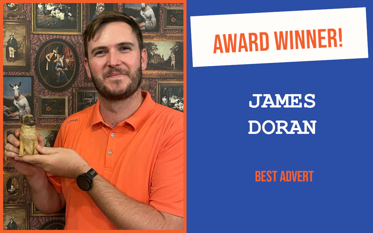 Close-up headshot of the winner of Leamington Spa's introductory question at the August networking event, wearing a bright orange t-shirt and holding the pug trophy, standing in front of a wall of small framed pictures.
