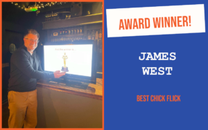 The winner of the introductory question at the October networking event in Chelmsford, standing in front of a screen with a trophy on it, pretending to hold the trophy.