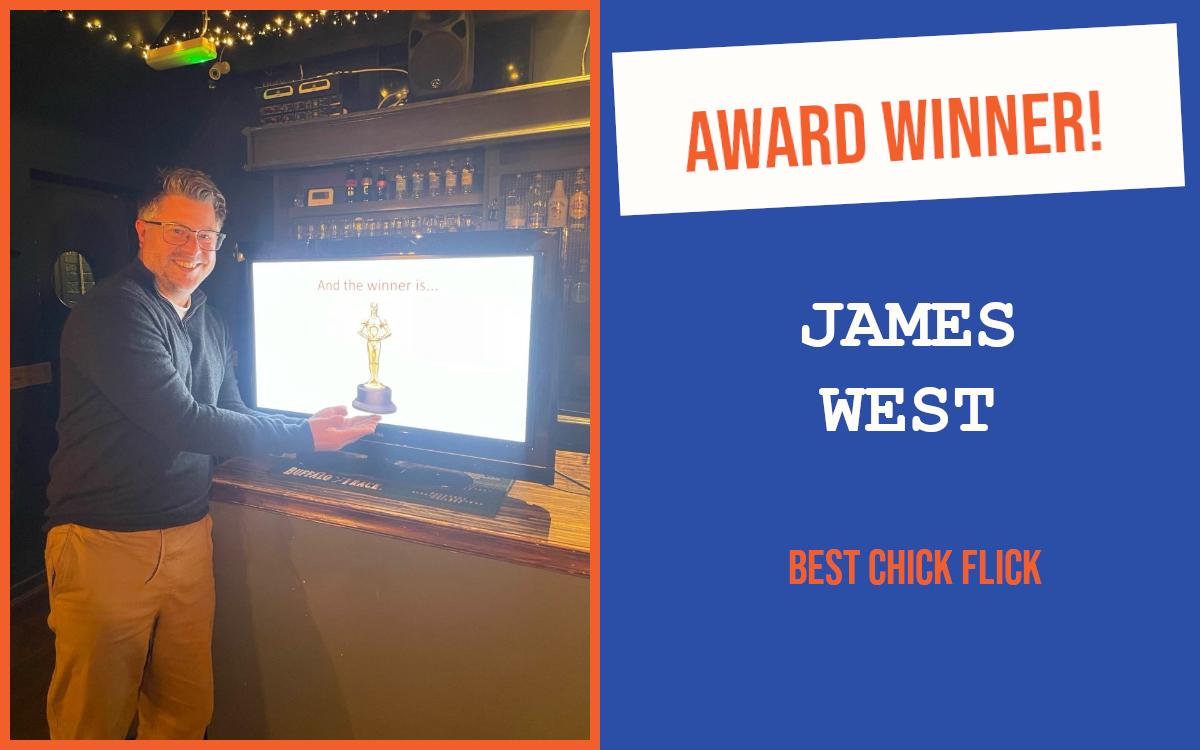 The winner of the introductory question at the October networking event in Chelmsford, standing in front of a screen with a trophy on it, pretending to hold the trophy.
